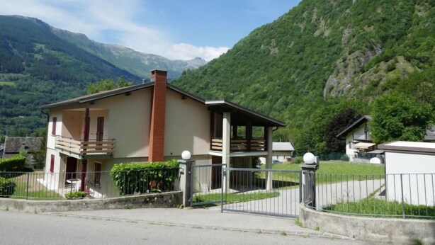 A two-story house with a balcony, surrounded by a fenced yard and set against a mountainous backdrop. - Vacation home Terry by Interhome (Olivone)