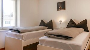A room with two single beds, a small bedside table with a lamp, and a painting on the wall. - Vacation home Terry by Interhome (Olivone)