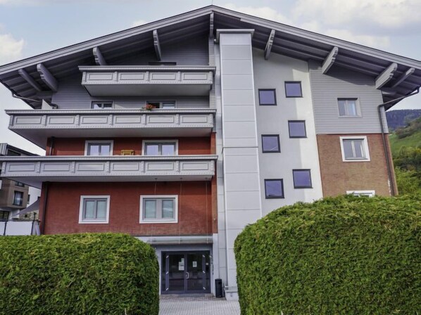Un edificio de varios pisos con una entrada central, balcones en los pisos superiores y una combinación de fachada de ladrillo y revestimiento.