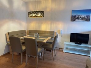 Una sala de estar moderna con un sofá, una mesa de comedor, sillas, un televisor de pantalla plana y un cuadro en la pared.