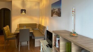Un soggiorno moderno con un divano, un tavolo da pranzo e una TV. Si nota una libreria con libri e un vaso di vetro decorativo.
