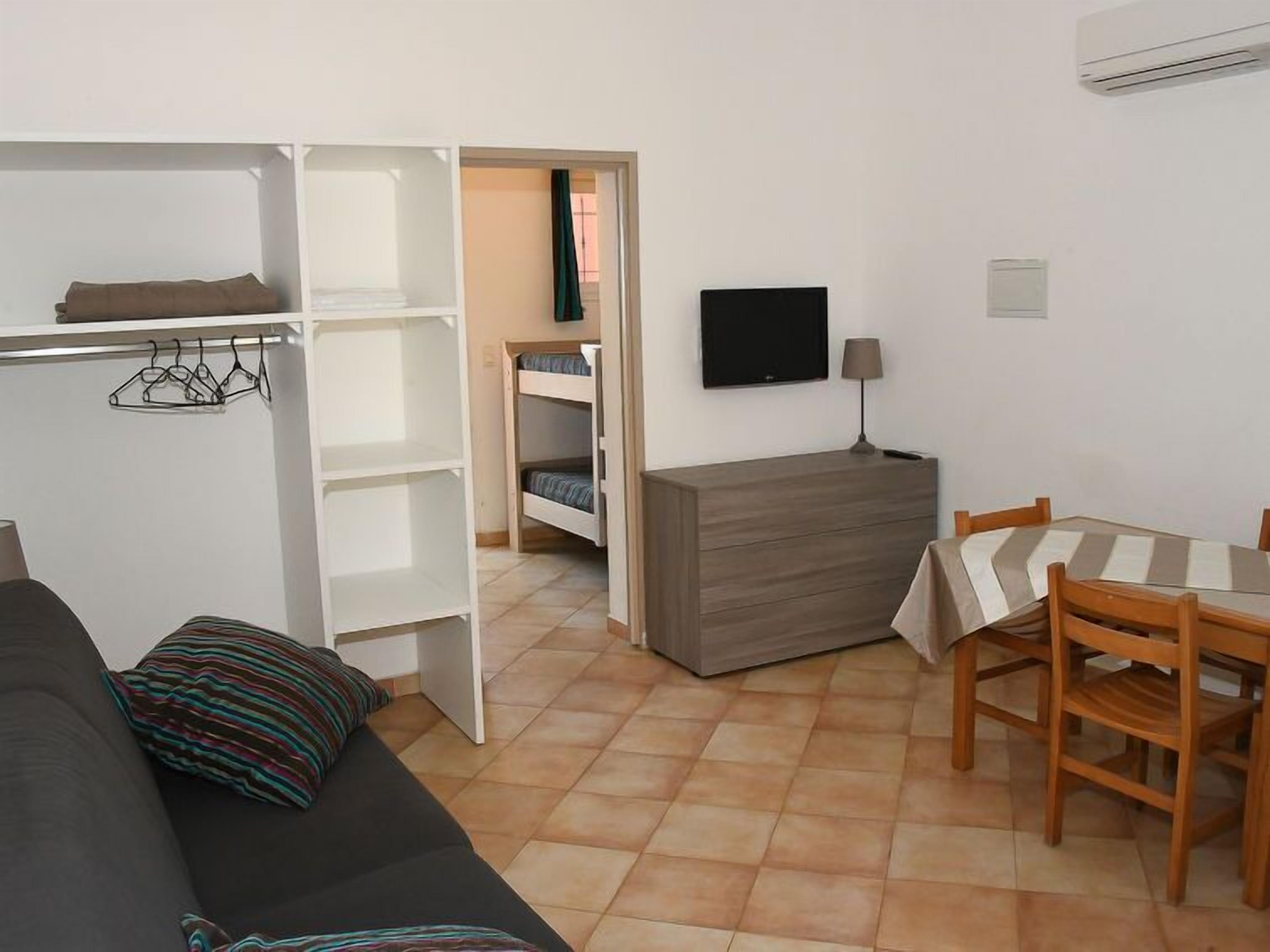 Una habitación pequeña con cama, escritorio, silla, televisor y armario.