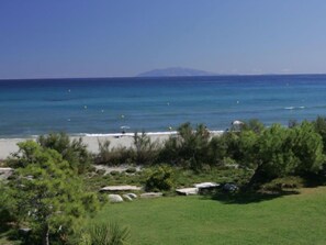 A beach with clear blue water, a distant mountain, and some greenery in the foreground. - Studio cabine Type B by Interhome (La Marana)