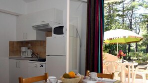 Un coin repas avec une table dressée pour deux personnes, une cuisine en arrière-plan et une vue sur les arbres et la verdure à l’extérieur.