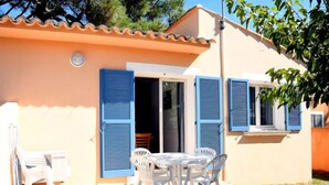 Una casa amb un pati enrajolat, una taula de dinar amb cadires i persianes blaves a les finestres.