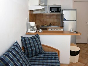 A compact kitchenette with a microwave, coffee maker, and refrigerator. There is a small seating area with a bench and pillows.