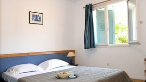 Un dormitori amb un llit, una tauleta de nit, una làmpada, una finestra amb cortines i un quadre al mur.