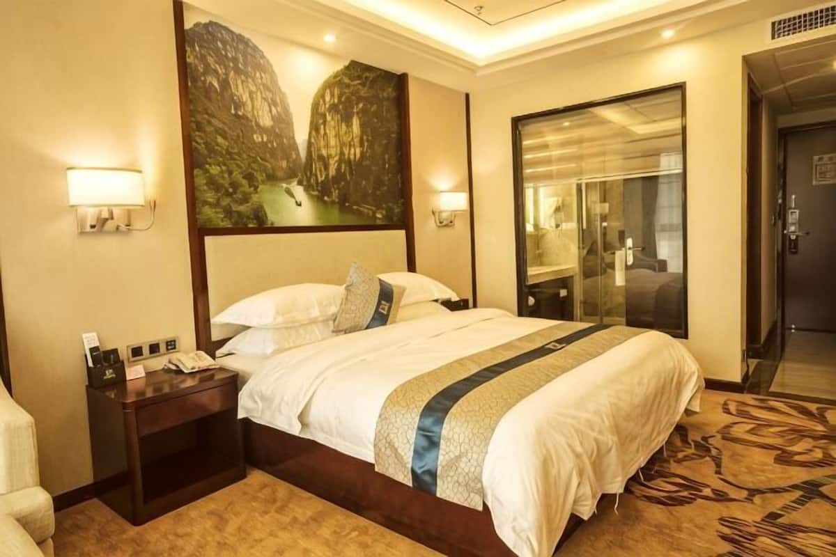A hotel room with a large bed, a nightstand with a phone, a painting on the wall, and a door to the bathroom.