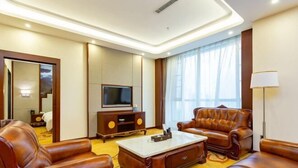 A hotel room with leather sofas, a flat-screen TV, a wooden cabinet, and a large window with curtains. - Tongxin Hotel (Zhenfeng)