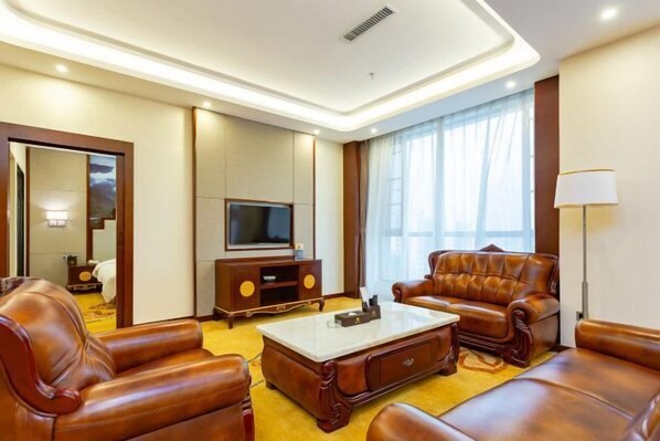 Ein Hotelzimmer mit Ledersofas, einem Flachbildfernseher, einem Holzschrank und einem großen Fenster mit Vorhängen.