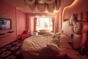 A bedroom with a large bed, a TV, a red chair, and a unique headboard design. - Tongxin Hotel (Zhenfeng)