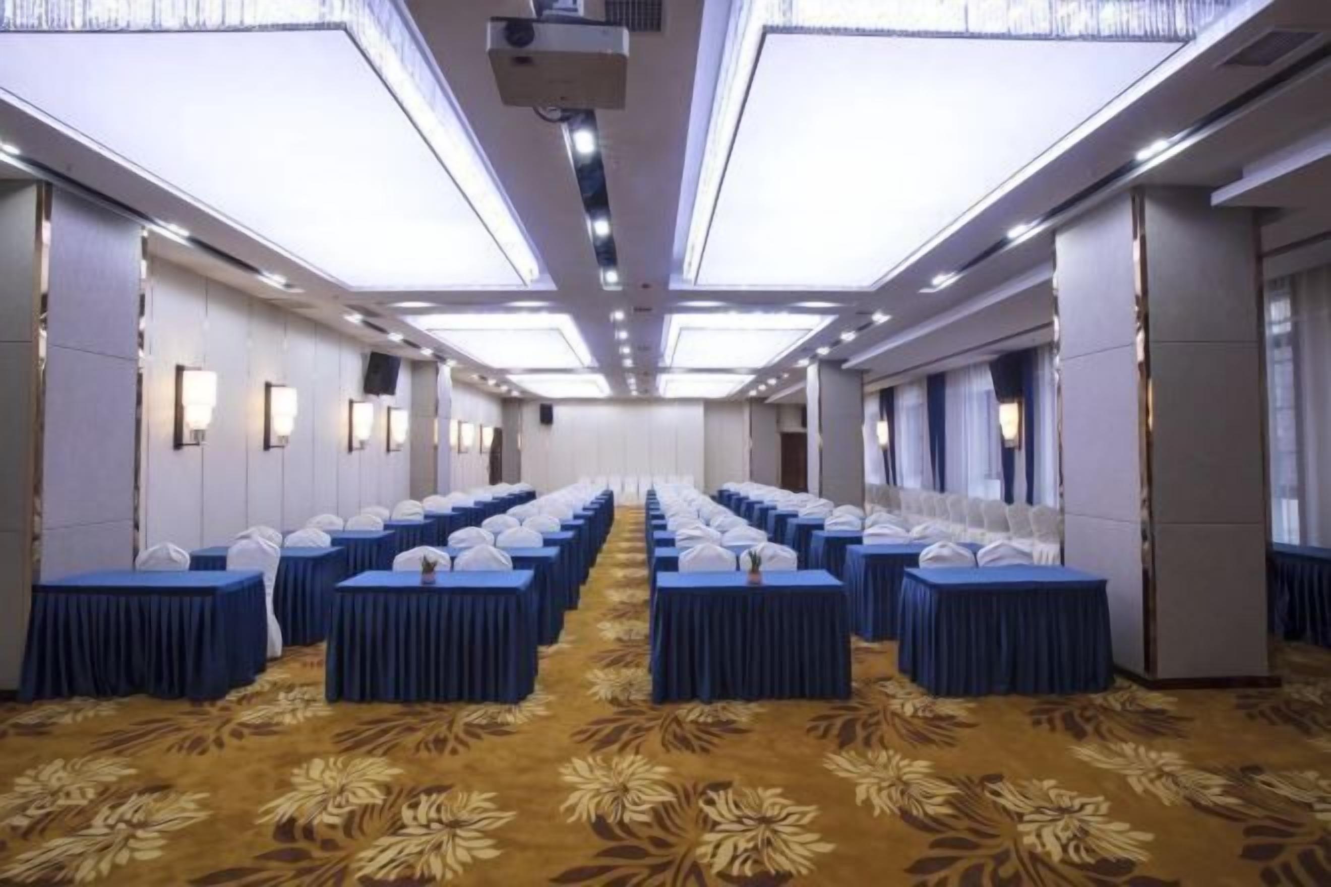 A conference room with rows of tables, a patterned carpet, and a high ceiling with recessed lighting.