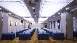 A conference room with rows of tables, a patterned carpet, and a high ceiling with recessed lighting. - Tongxin Hotel (Zhenfeng)
