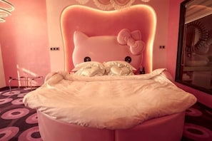 A bed with a Hello Kitty headboard, a circular light fixture, and a mirror on the wall. - Tongxin Hotel (Zhenfeng)