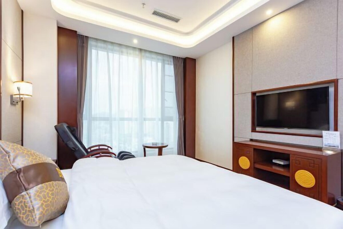 A hotel room with a large bed, a flat-screen TV, a small table, and a chair.