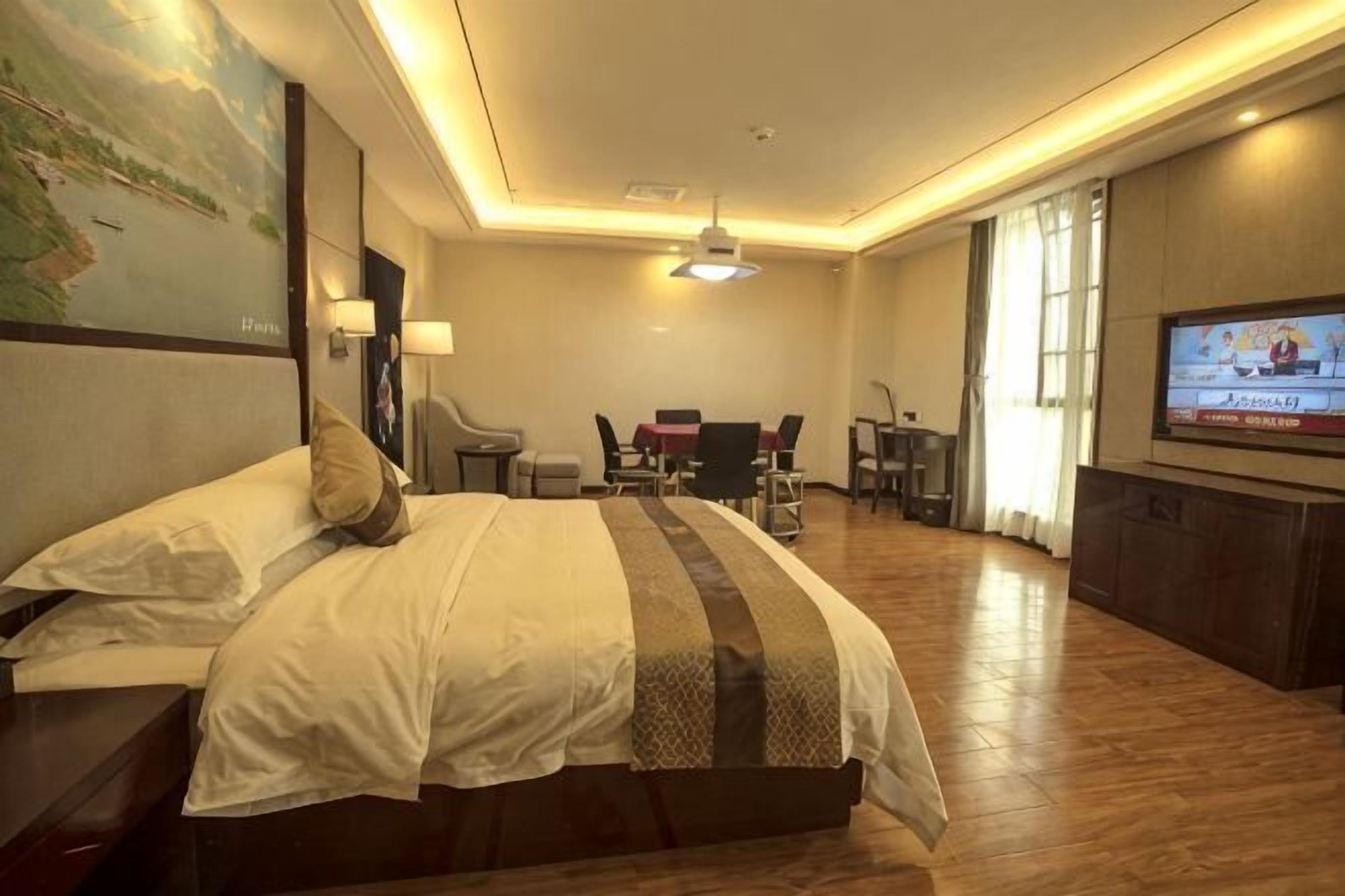 A hotel room with a bed, a desk, a television, and a dining area.