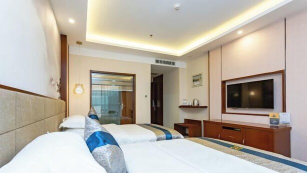 A hotel room with two beds, a TV, a desk, and a bathroom visible through a glass door. - Tongxin Hotel (Zhenfeng)