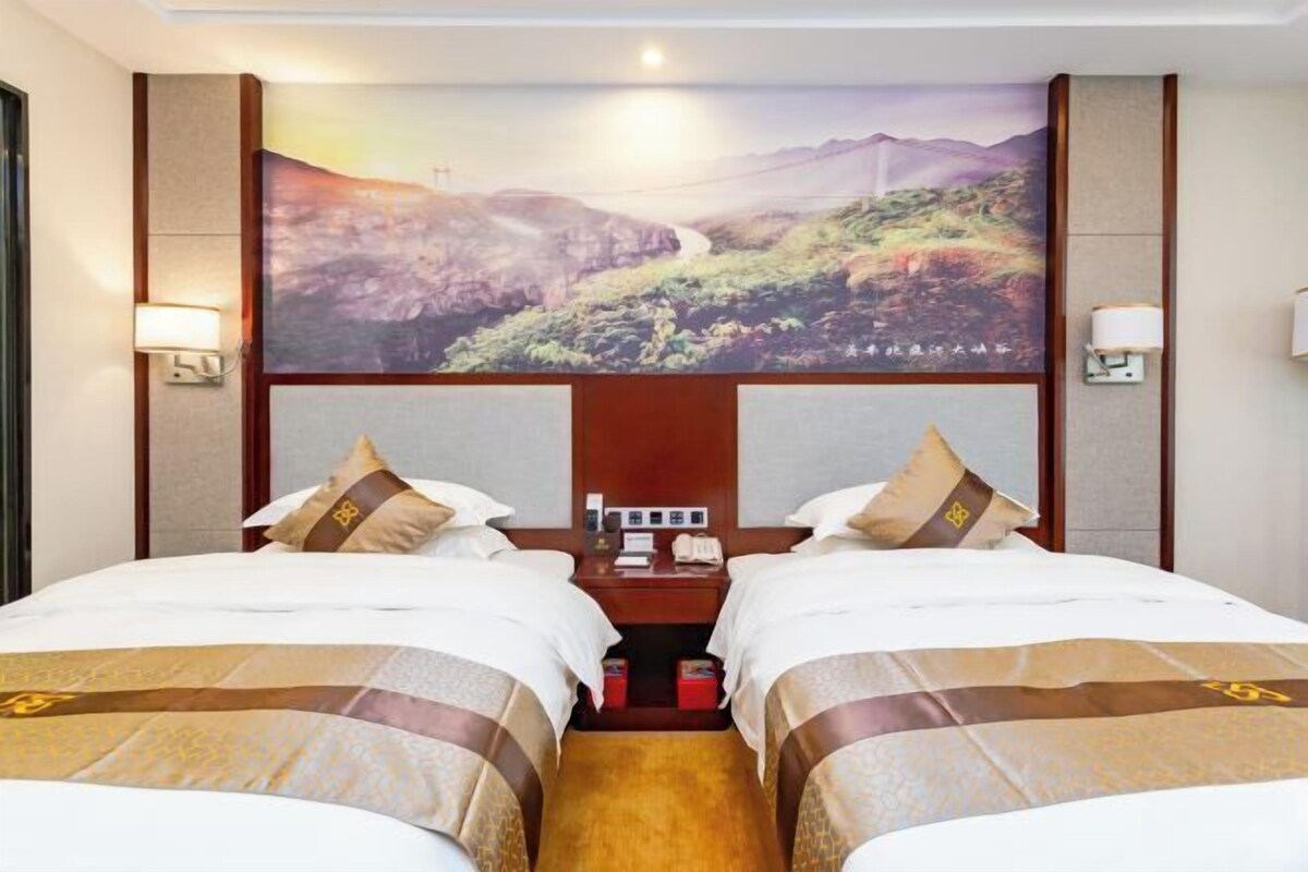 A hotel room with two beds, a large wall-mounted TV, and a nightstand with a phone and a lamp.