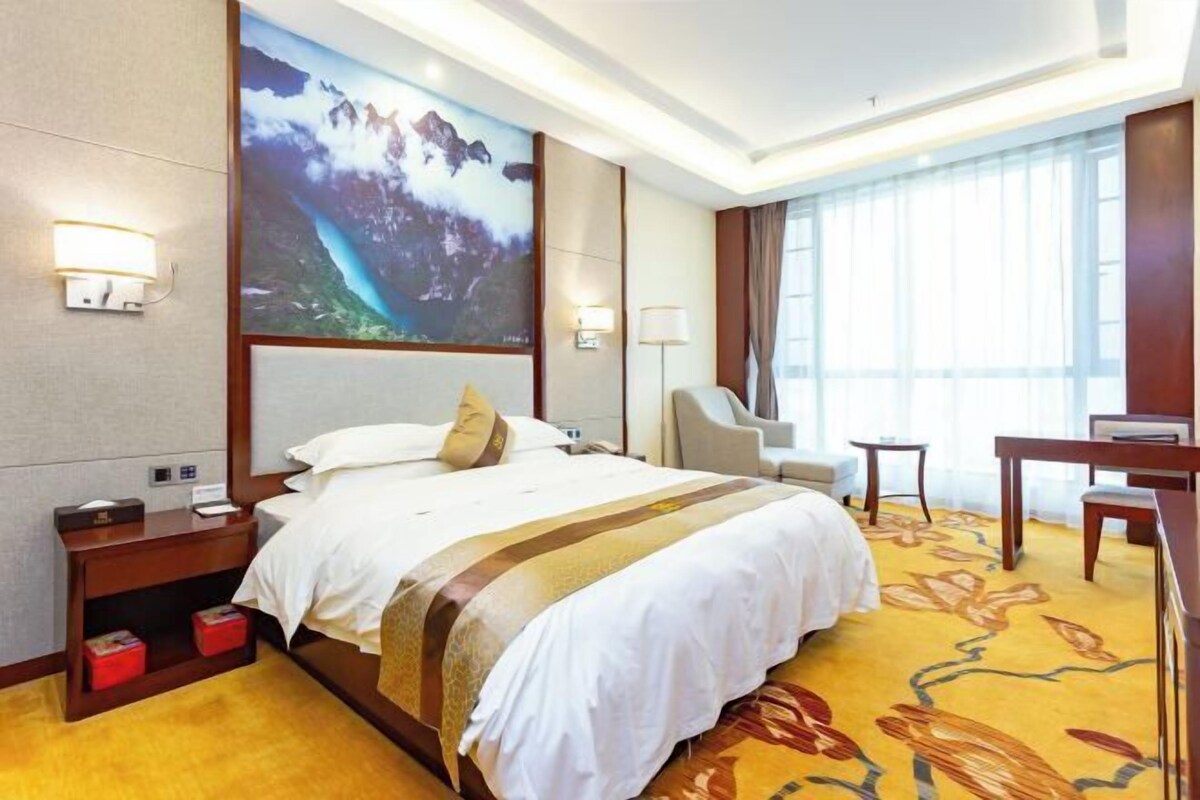 A hotel room with a large bed, a desk, a chair, and a TV.