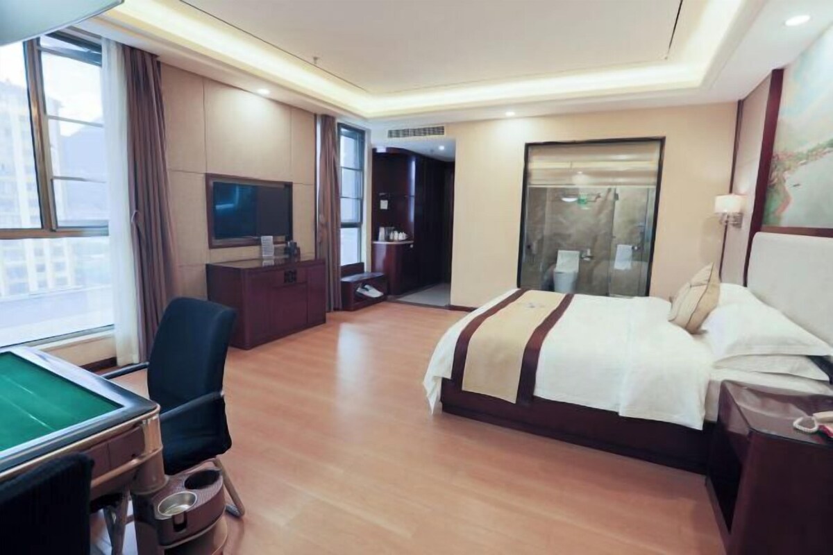 A hotel room with a bed, desk, chair, and a television.