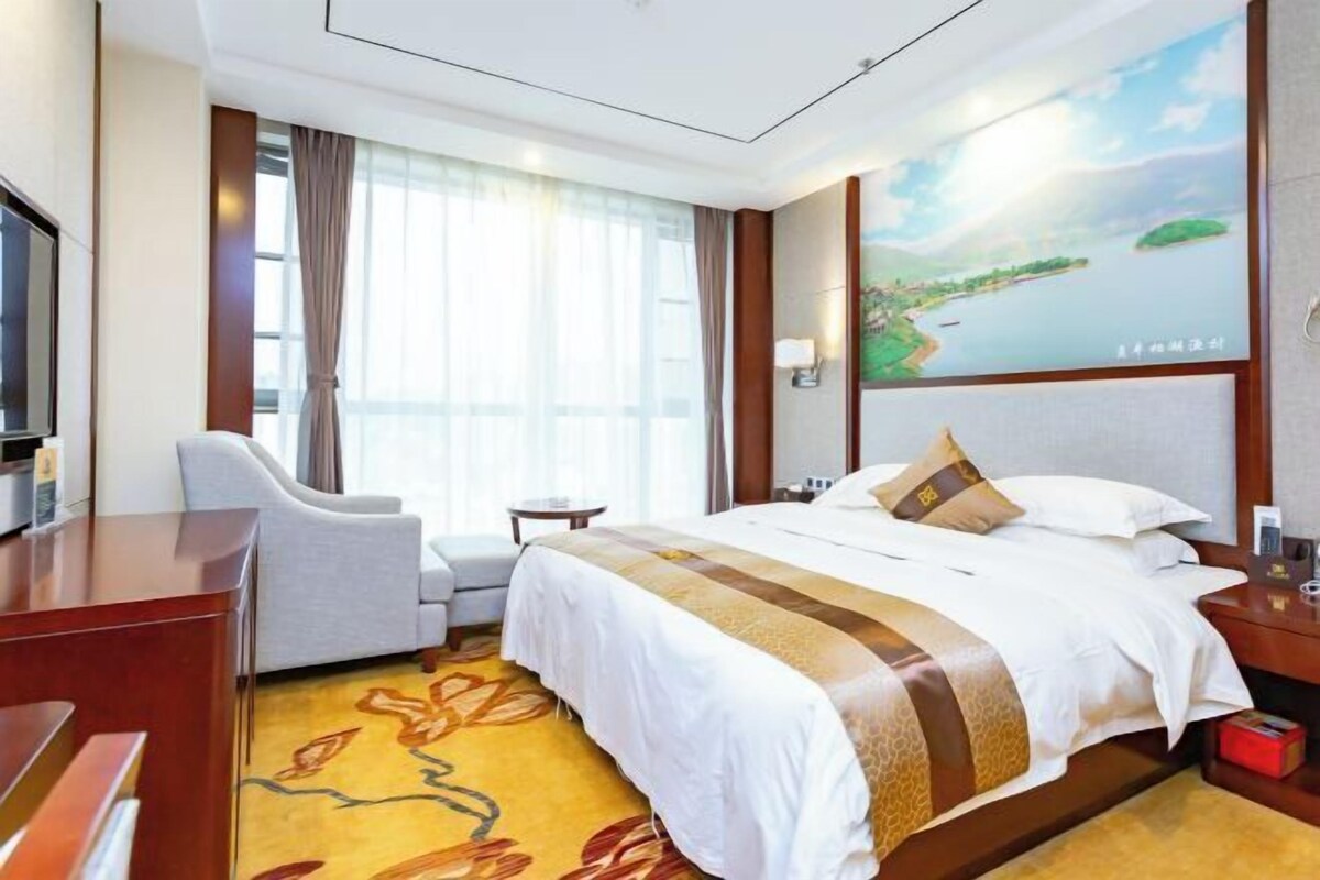 A hotel room with a bed, a desk, a chair, a TV, and a painting on the wall.