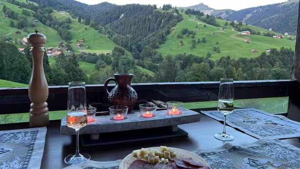 A table with a cheese platter, glasses, a pitcher, and candles, overlooking a mountainous landscape. - Serviced Apartment Chalet Bärgblüml i Ha by Interhome (Habkern)