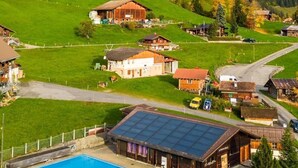 A rural area with a swimming pool, houses, and a forested hill. - Serviced Apartment Chalet Bärgblüml i Ha by Interhome (Habkern)