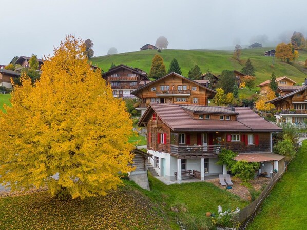 A traditional chalet-style building with a balcony, surrounded by lush greenery and autumn foliage.