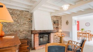 A cozy living room with a stone wall, a fireplace, wooden furniture, and a dining area in the background. - Le havre de paix by Interhome (Créances)
