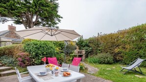 A white table with chairs and a beige umbrella, surrounded by lush greenery and a wooden deck. - Le havre de paix by Interhome (Créances)