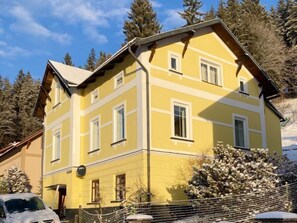 A yellow multi-story building with white trim, a sloped roof, and multiple windows.