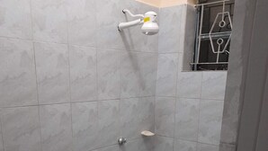 Un bagno piccolo rivestito di piastrelle, con il water, una cabina doccia e una finestra con inferriate.