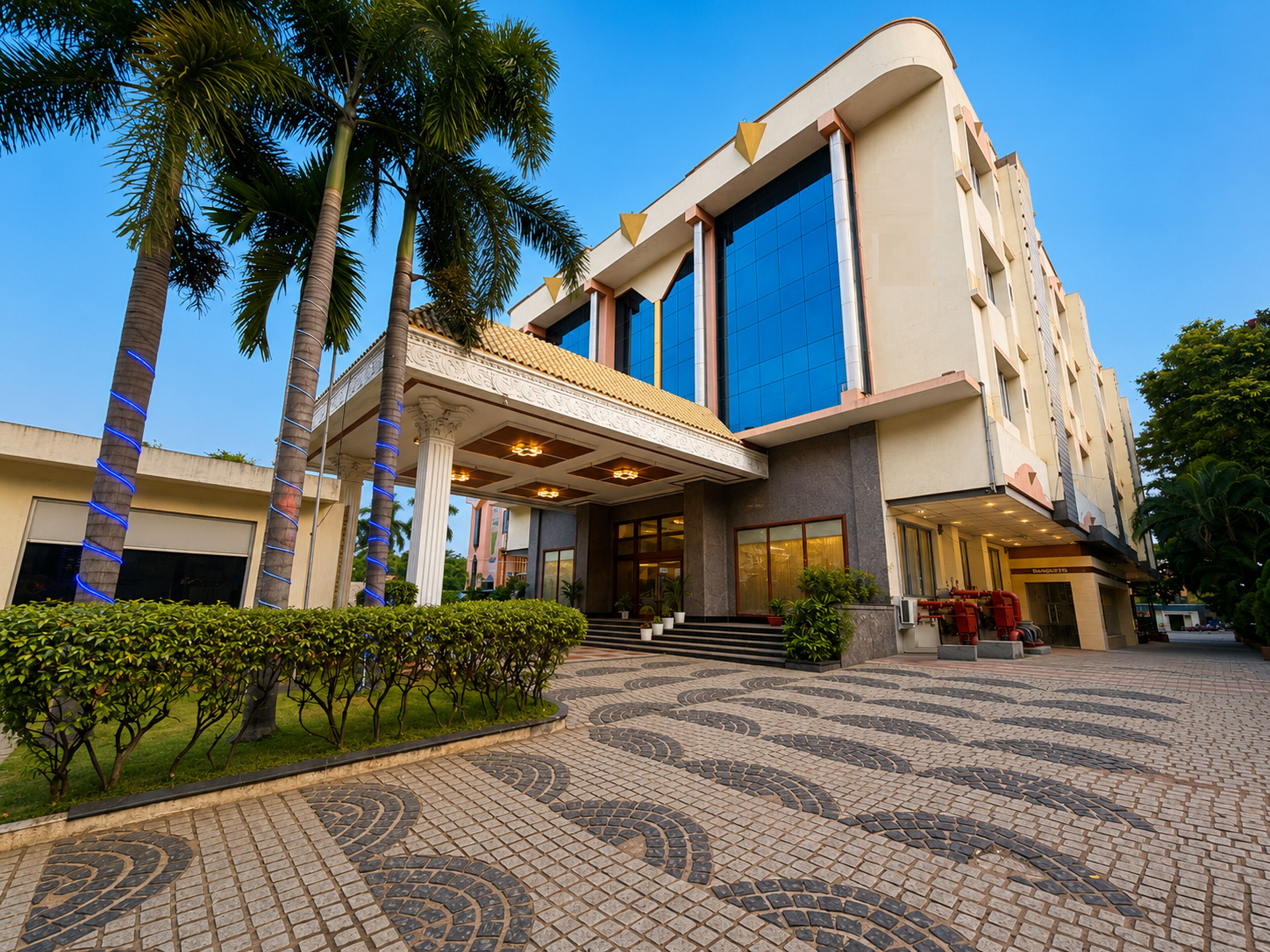 A modern hotel with a covered entrance, palm trees, and a patterned pavement.