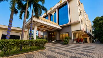 A modern hotel with a covered entrance, palm trees, and a patterned pavement.