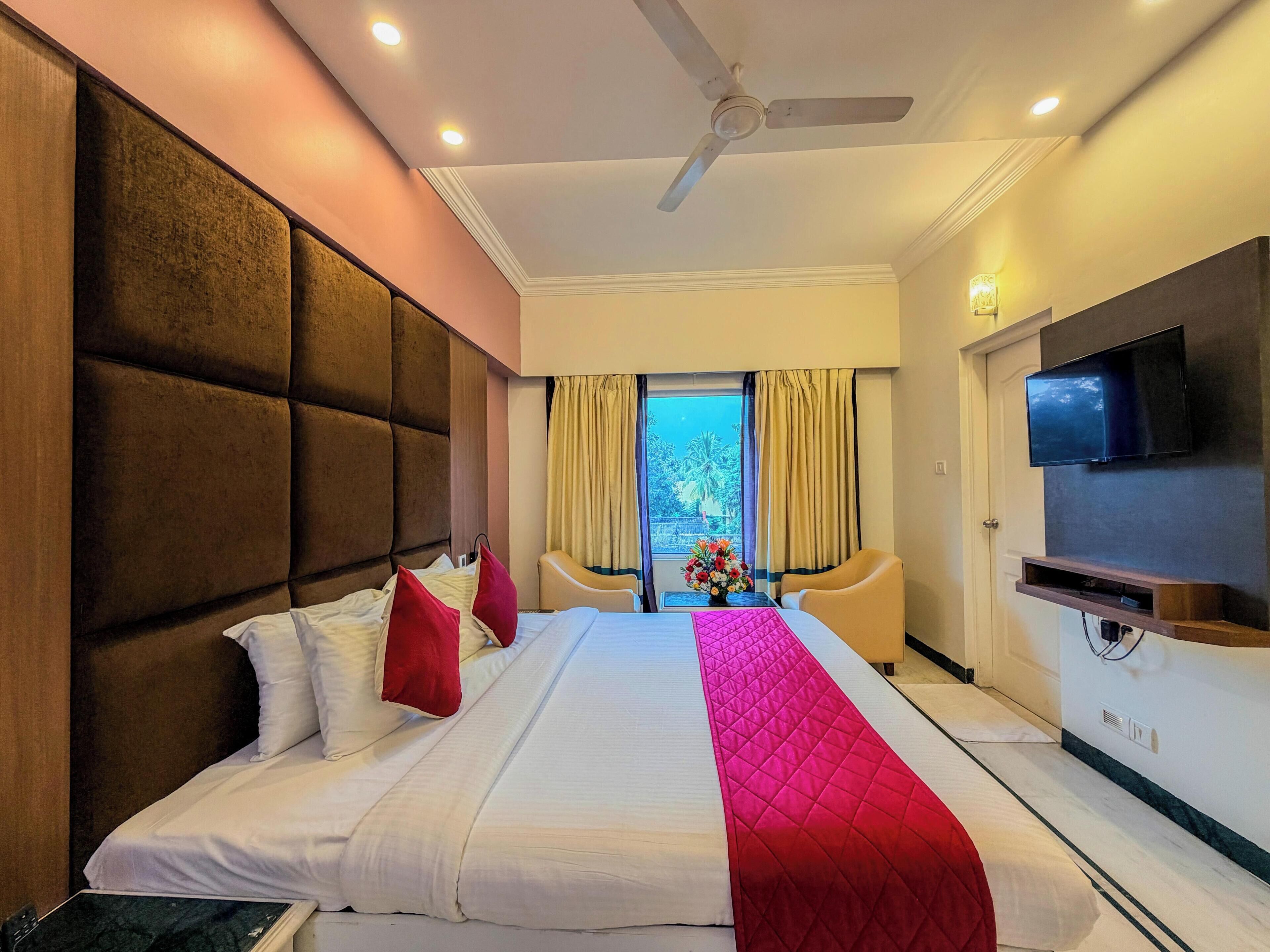 A hotel room with a large bed, a ceiling fan, a TV, and a view of the outdoors.