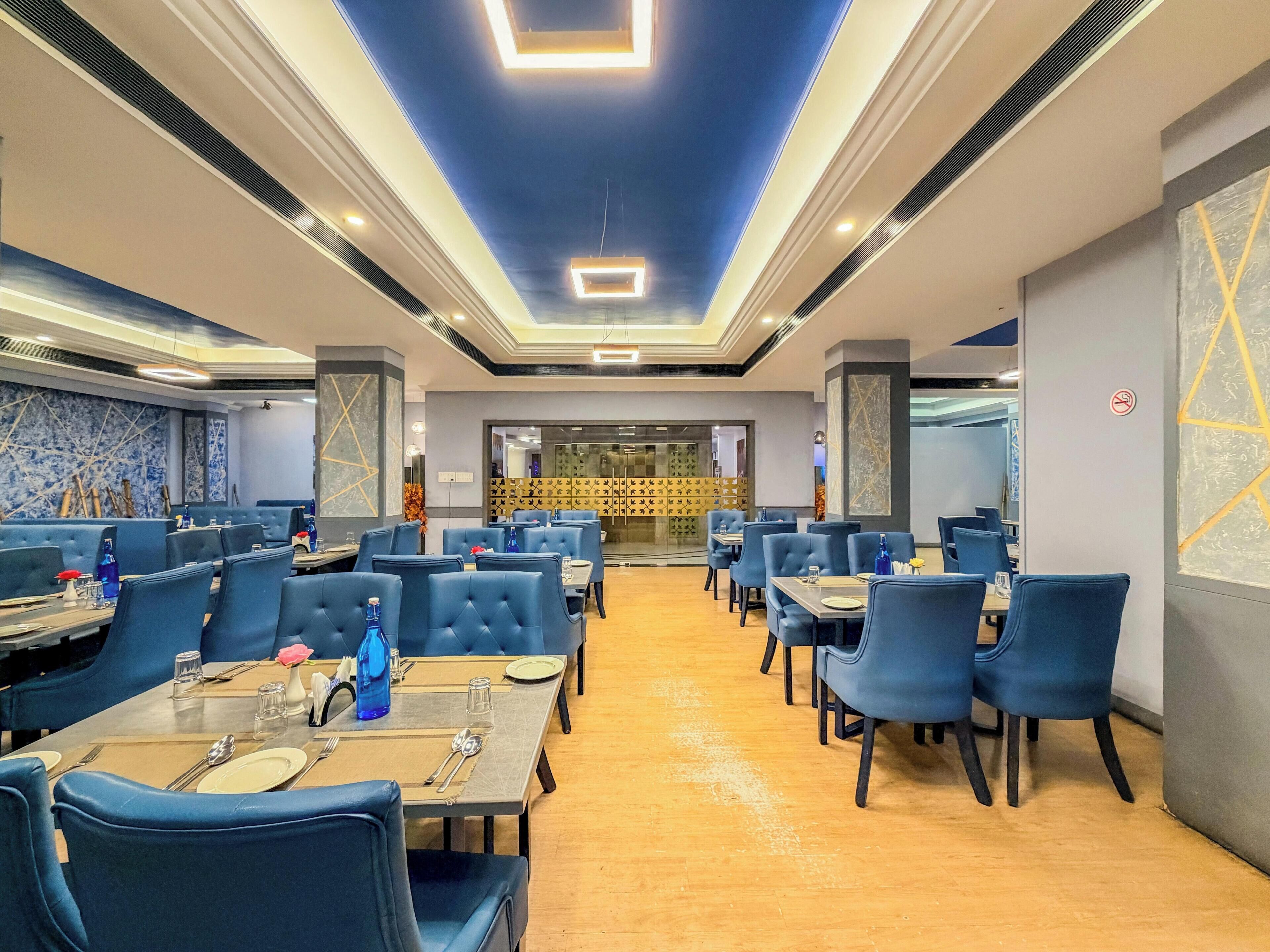 A restaurant with blue upholstered booths and tables, a wooden floor, and a blue ceiling with recessed lighting.