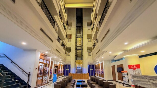 A hotel lobby with a central staircase, seating area, and a reception desk. - Zip By Spree Hotels Surabi International Vellore (Vellore)