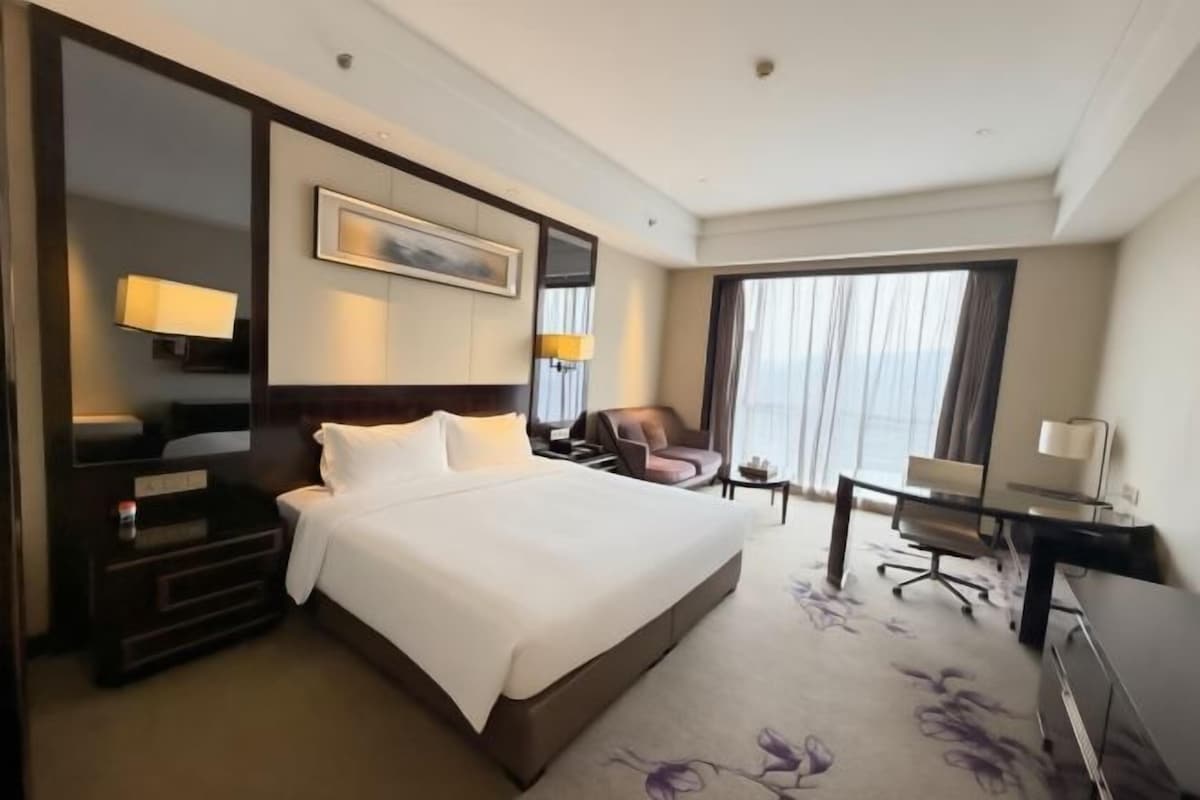 A hotel room with a large bed, a desk, a chair, a TV, and a window with curtains.