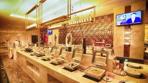 Un espace buffet doté de plusieurs présentoirs de nourriture, d’un téléviseur fixé au mur et d’un sol en marbre.