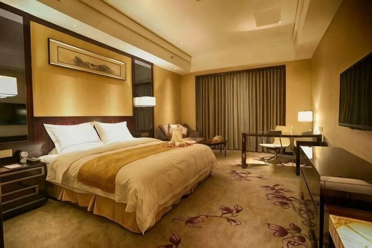 Une chambre d’hôtel avec un grand lit, un bureau, une chaise, une télévision et une fenêtre avec des rideaux.