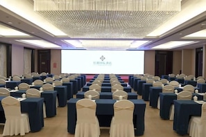 Un salón de conferencias con filas de mesas y sillas, una pantalla de proyector y una araña.