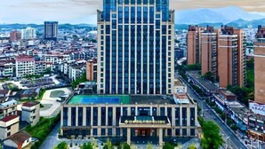 Un hôtel moderne, reconnaissable à son grand panneau « GUIDU », entouré de bâtiments urbains et dominé par un paysage montagneux.