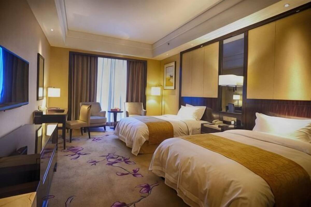 Une chambre d’hôtel avec deux lits, un bureau, une chaise, une lampe et une grande fenêtre avec des rideaux.