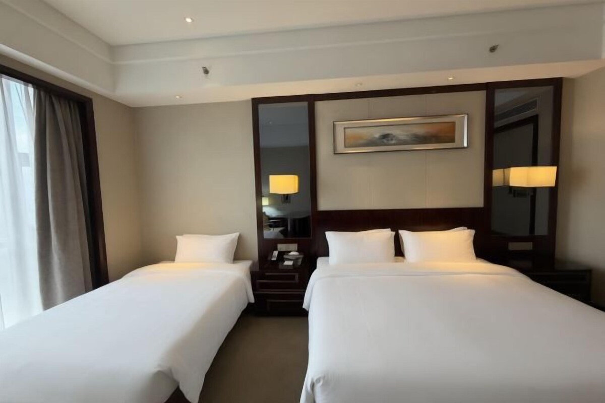 A hotel room with two beds, a nightstand, a lamp, and a painting on the wall.