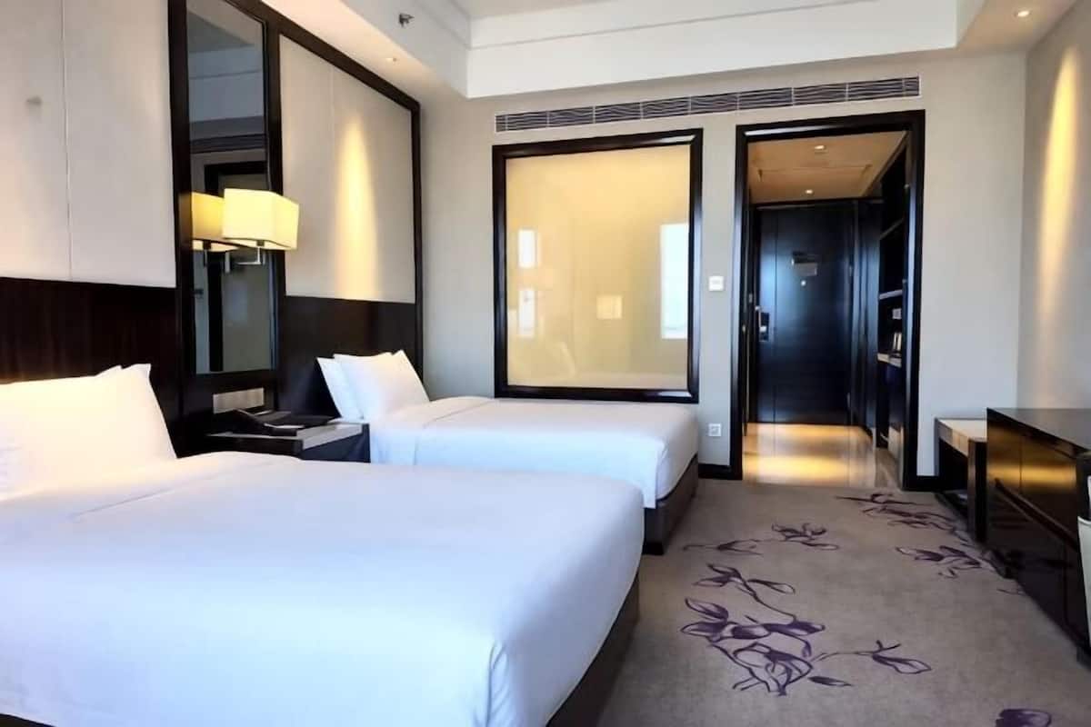 Une chambre d’hôtel avec deux lits, un bureau, une chaise, une lampe et un grand miroir.