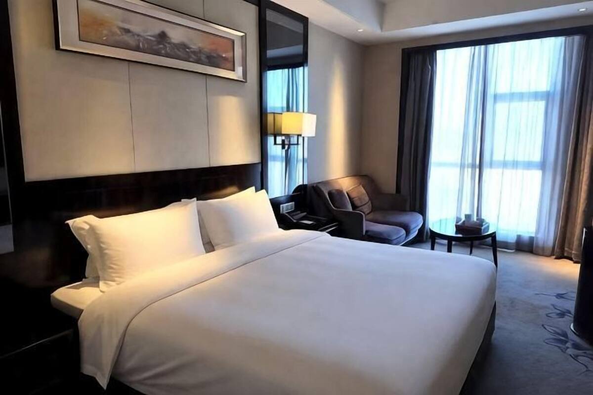Une chambre d’hôtel avec un grand lit, une chaise, une petite table et une fenêtre avec des rideaux.