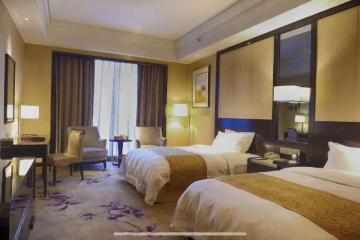 Habitación de hotel con dos camas, un escritorio, una silla, una mesita y un espejo grande.