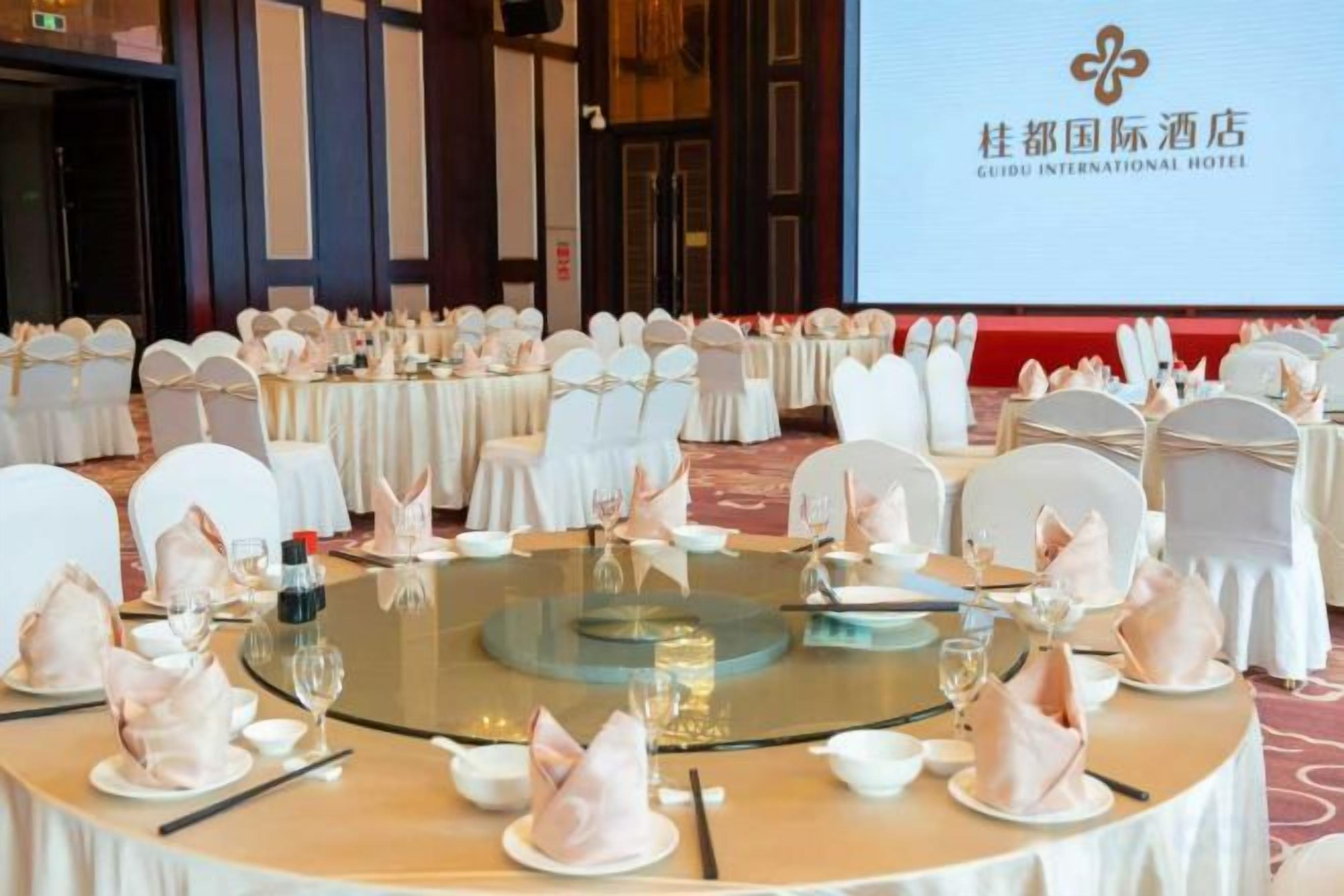 Une salle de banquet avec des tables rondes dressées pour un événement formel, et un grand écran en arrière-plan affichant l’image de marque de l’hôtel.