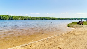 Una spiaggia sabbiosa con una panchina di legno e una ringhiera metallica.