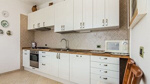 A modern kitchen with white cabinets, a stainless steel oven, a microwave, and a wooden countertop.